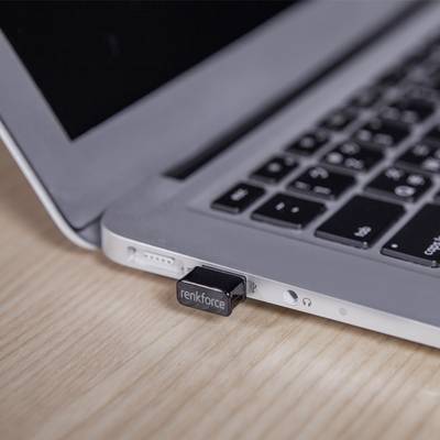 Une clé USB de renkforce est branchée sur un ordinateur portable qui se trouve sur une table en bois. Une partie du clavier de l'ordinateur portable est visible.