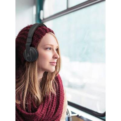 Une femme portant des écouteurs est assise dans un bus et regarde par la fenêtre. Elle porte une écharpe rouge et un bonnet. Vue extérieure floue.