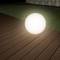 Une sphère lumineuse sur une terrasse en bois à côté d'une pelouse, lors d'une prise de vue nocturne.