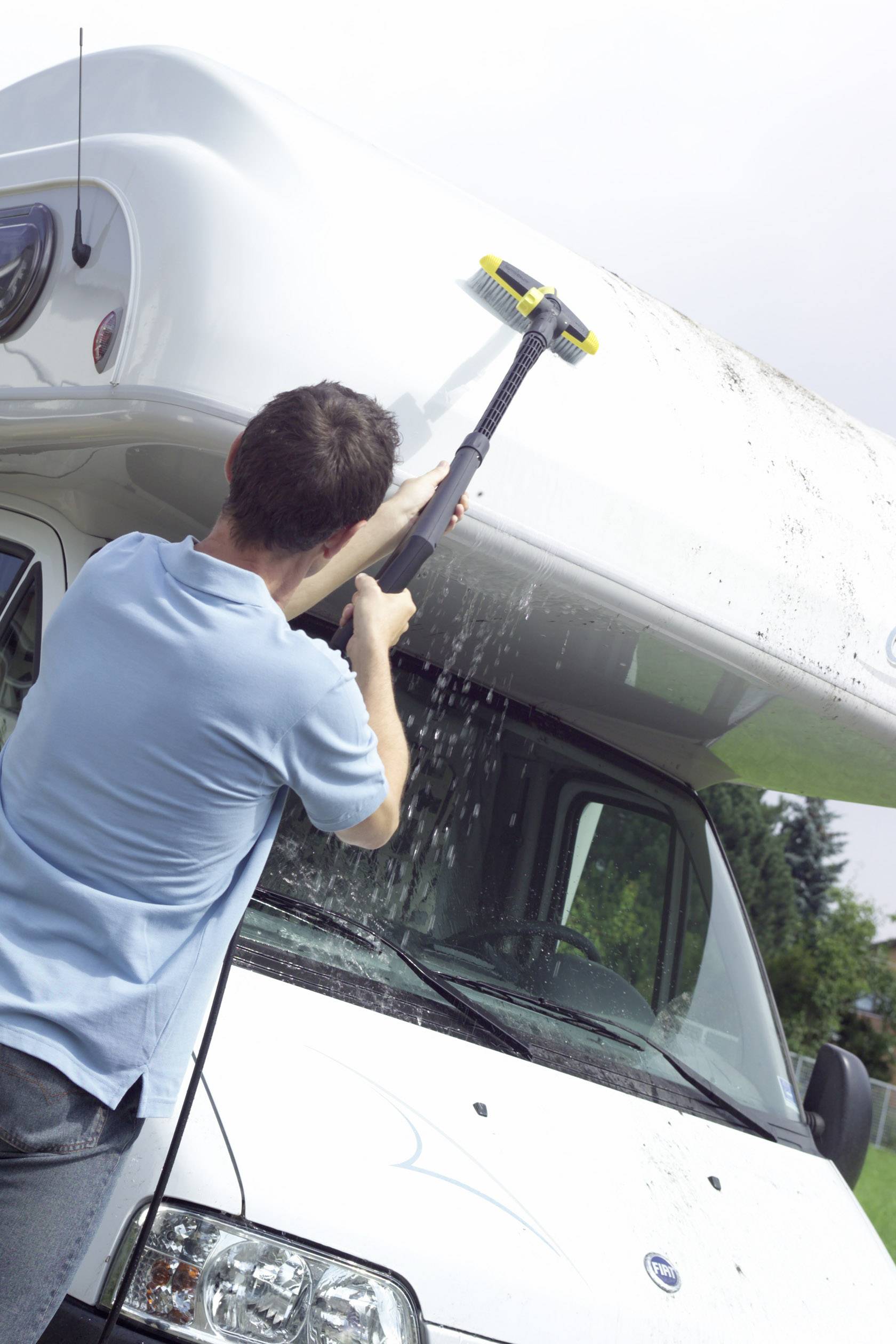 Une personne nettoie le toit d'un camping-car avec un nettoyeur haute pression. L'eau gicle pendant que les saletés sont éliminées.
