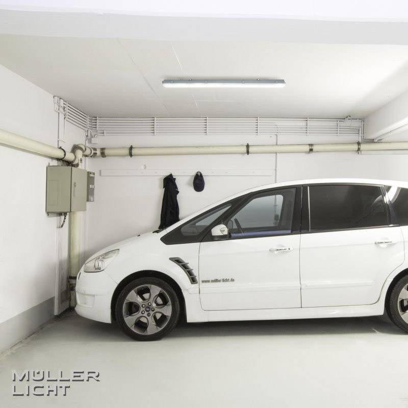 Une voiture blanche est garée dans un garage fermé. Un dispositif d'éclairage se trouve en haut à gauche.