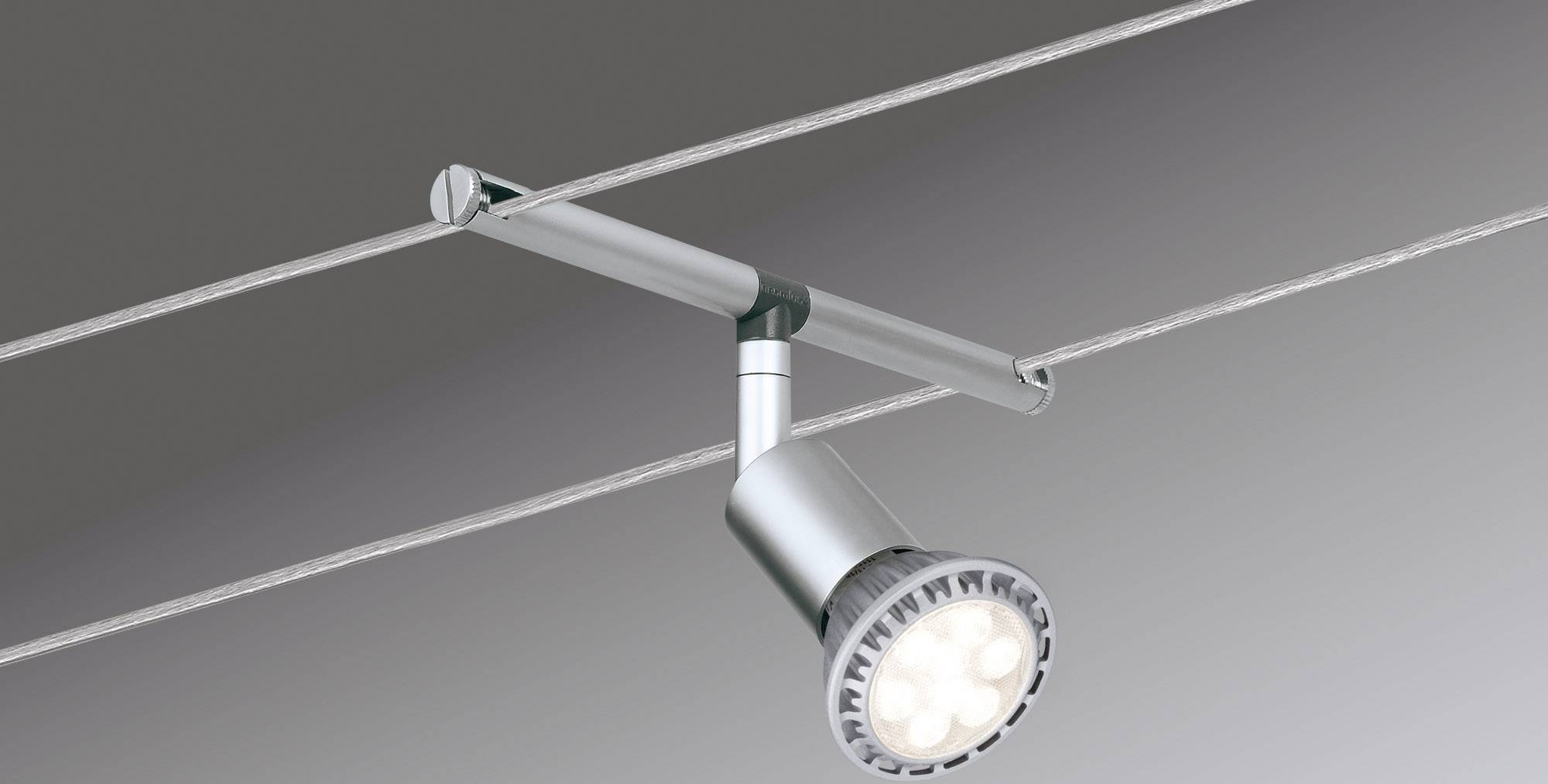 Un projecteur argenté fixé à des câbles est suspendu et diffuse une lumière vive. Idéal pour un éclairage ciblé dans des espaces de vie modernes.