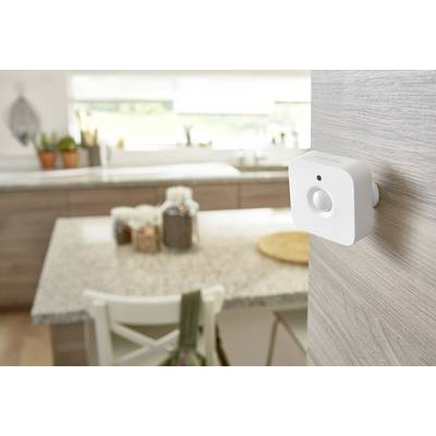 Un détecteur de mouvement est installé sur un mur en bois dans une cuisine moderne. En arrière-plan, une table est garnie de contenants de stockage.