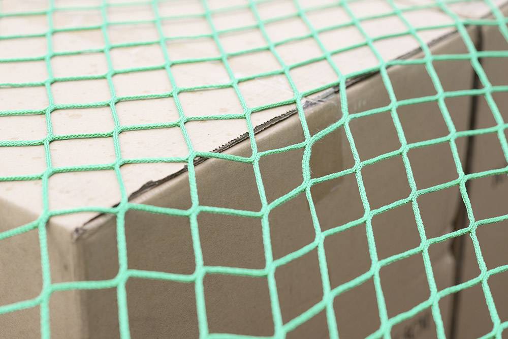 Un carton sécurisé par un filet vert. Le filet est tendu fermement et recouvre toute la surface du carton.