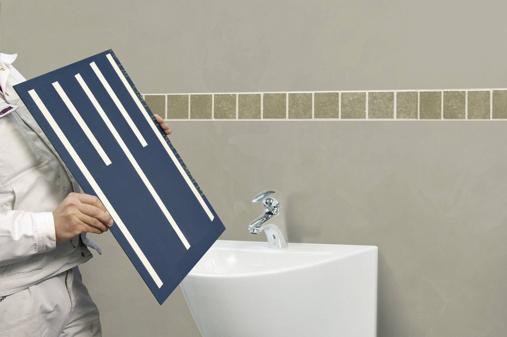 Une personne tient un pochoir à carreaux avec des bandes régulières devant un mur recouvert de carreaux rectangulaires disposés en diagonale, au-dessus d'un lavabo.
