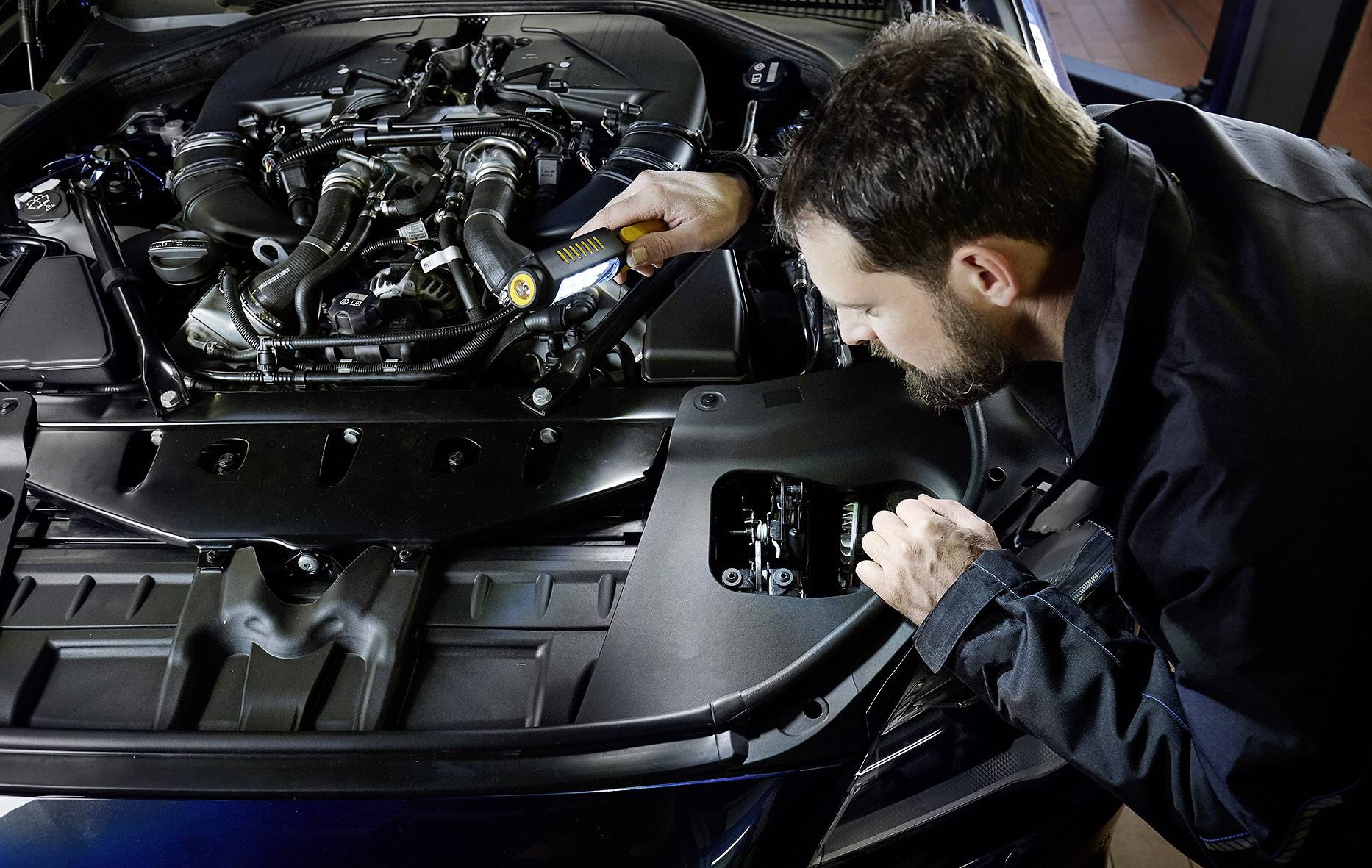 Un mécanicien vérifie le moteur d'une voiture dans un environnement d'atelier. Il utilise une lampe de poche pour mieux voir.