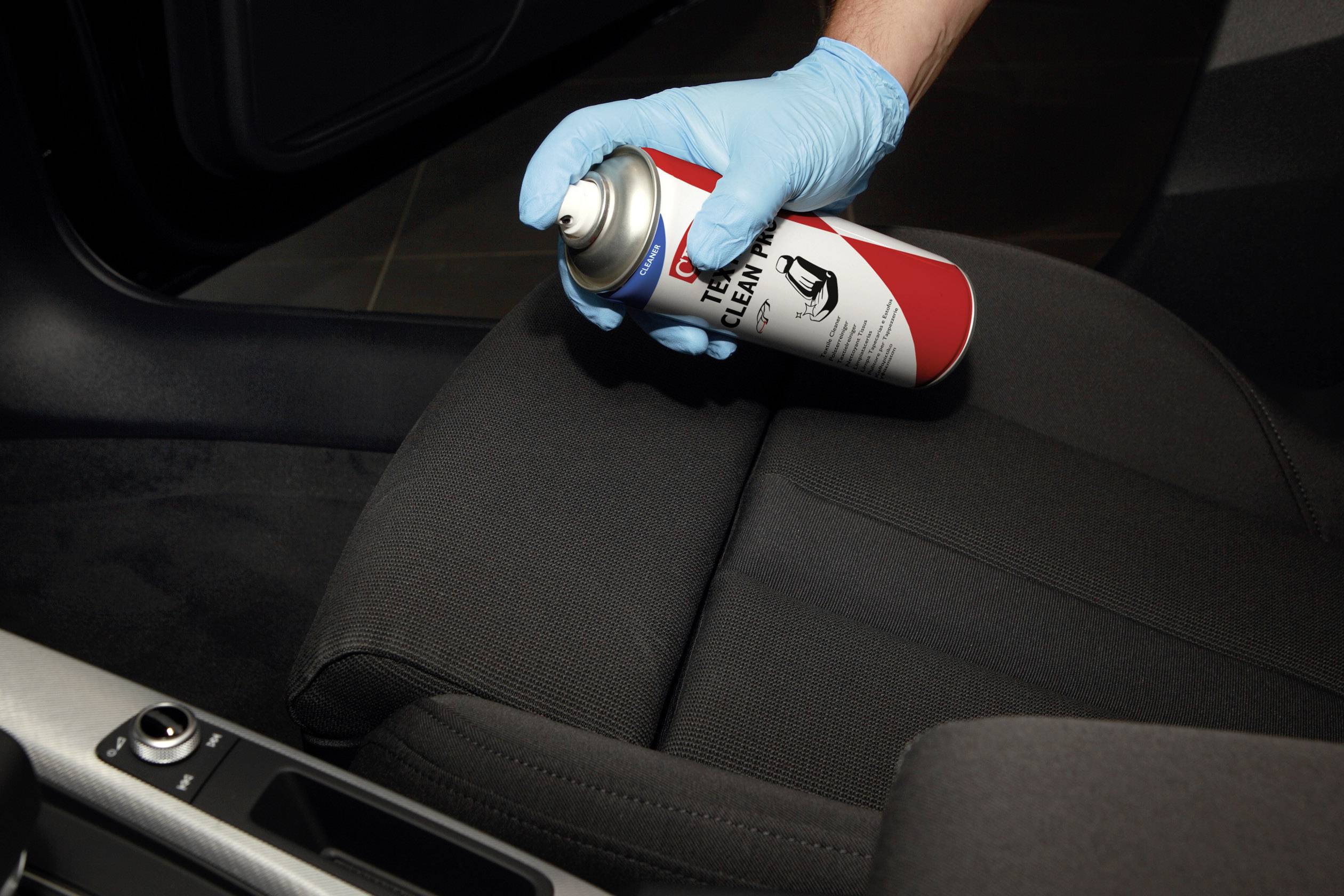 Une personne portant des gants vaporise un produit nettoyant à partir d'un aérosol sur un siège de voiture pour le nettoyer ou l'entretenir.