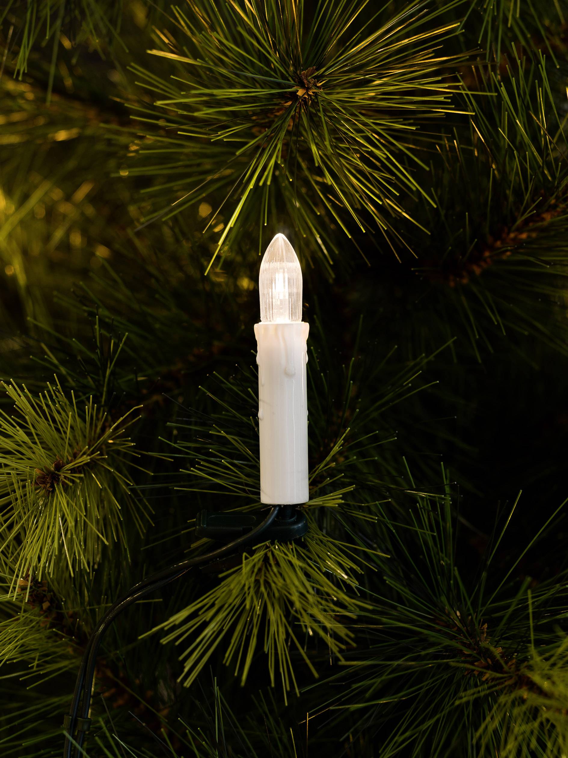 Une bougie électrique brille entre des branches de sapin vert. Elle diffuse une lumière chaleureuse et contribue à créer une atmosphère festive.