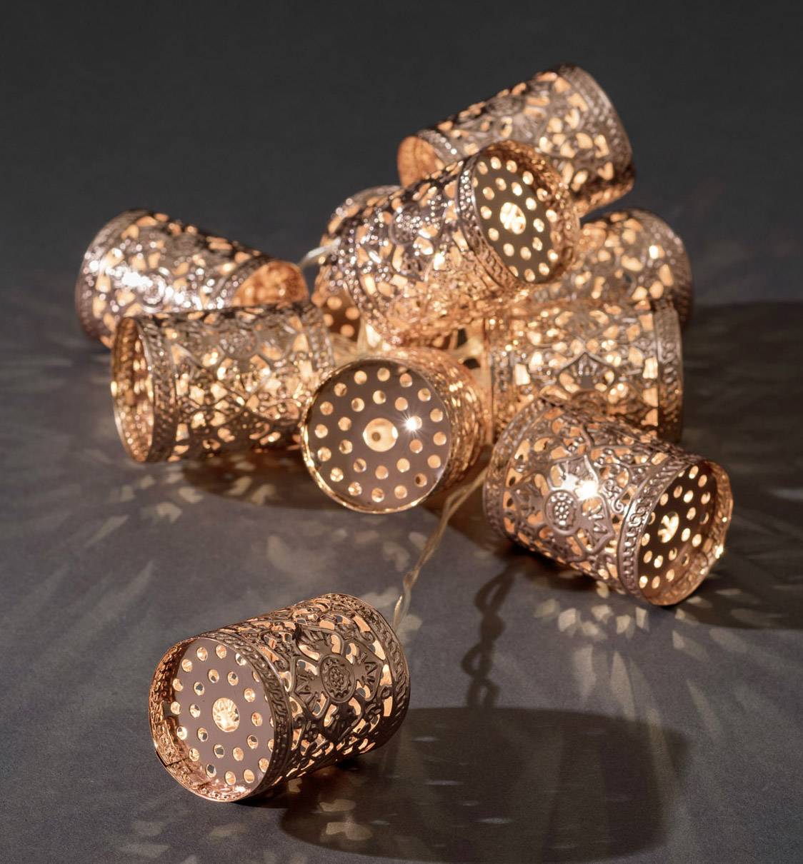 Une série de guirlandes lumineuses décoratives au design filigrane et ajouré, diffusant une lumière chaleureuse sur un fond sombre.