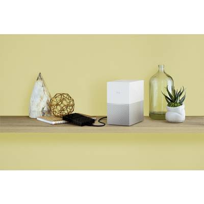 Un bureau décoré, avec un disque dur externe, un smartphone et des plantes devant un mur jaune.
