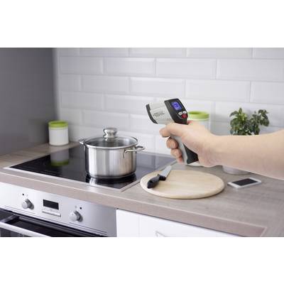 Une personne pointe un thermomètre infrarouge au-dessus d'une casserole sur une cuisinière pour vérifier la température pendant la cuisson.
