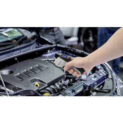 Une main tient un thermomètre numérique au-dessus du compartiment moteur ouvert d'une voiture pour mesurer la température.