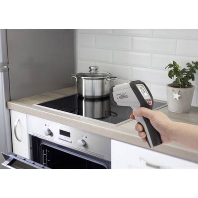 Une main tient un thermomètre infrarouge et mesure la température d'une casserole sur une plaque de cuisson à induction dans une cuisine moderne.