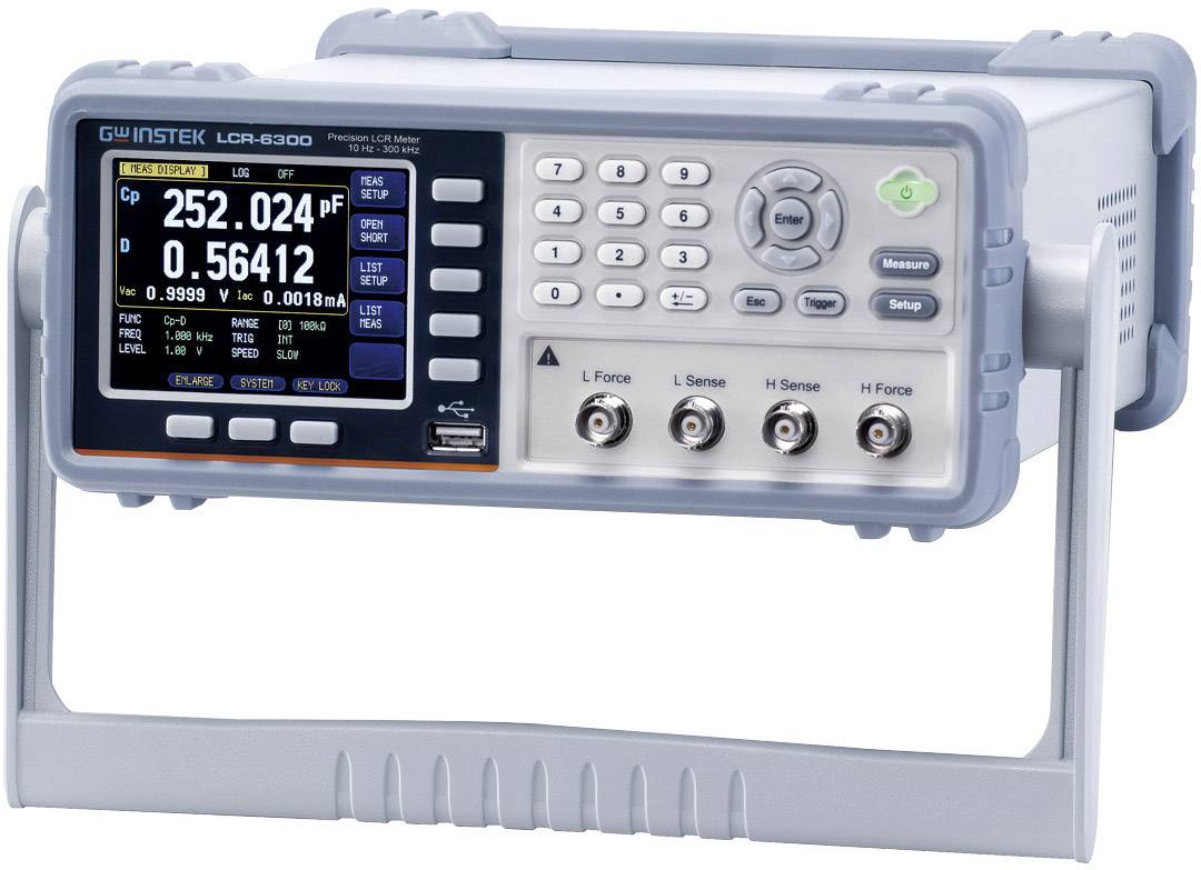 Un appareil de mesure LCR doté d'un écran numérique affiche la capacité, l'impédance et le facteur de perte. Des boutons de réglage et quatre bornes de connexion sont visibles.