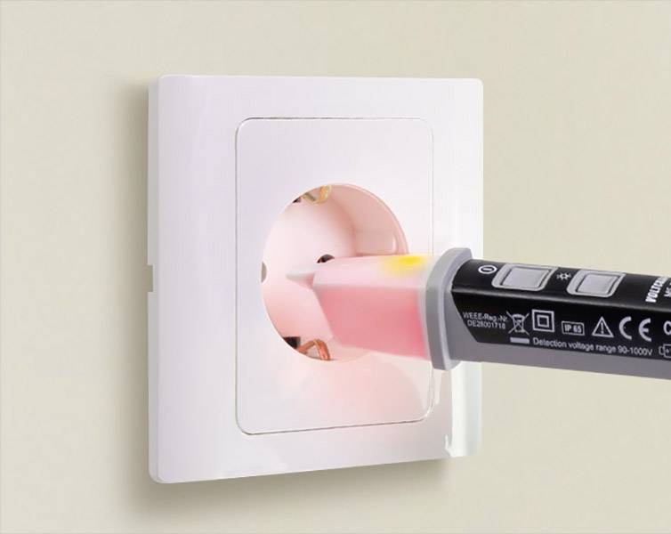 Un testeur de tension s'allume en rouge lorsqu'il est inséré dans une prise électrique blanche, ce qui indique la présence d'une tension électrique.