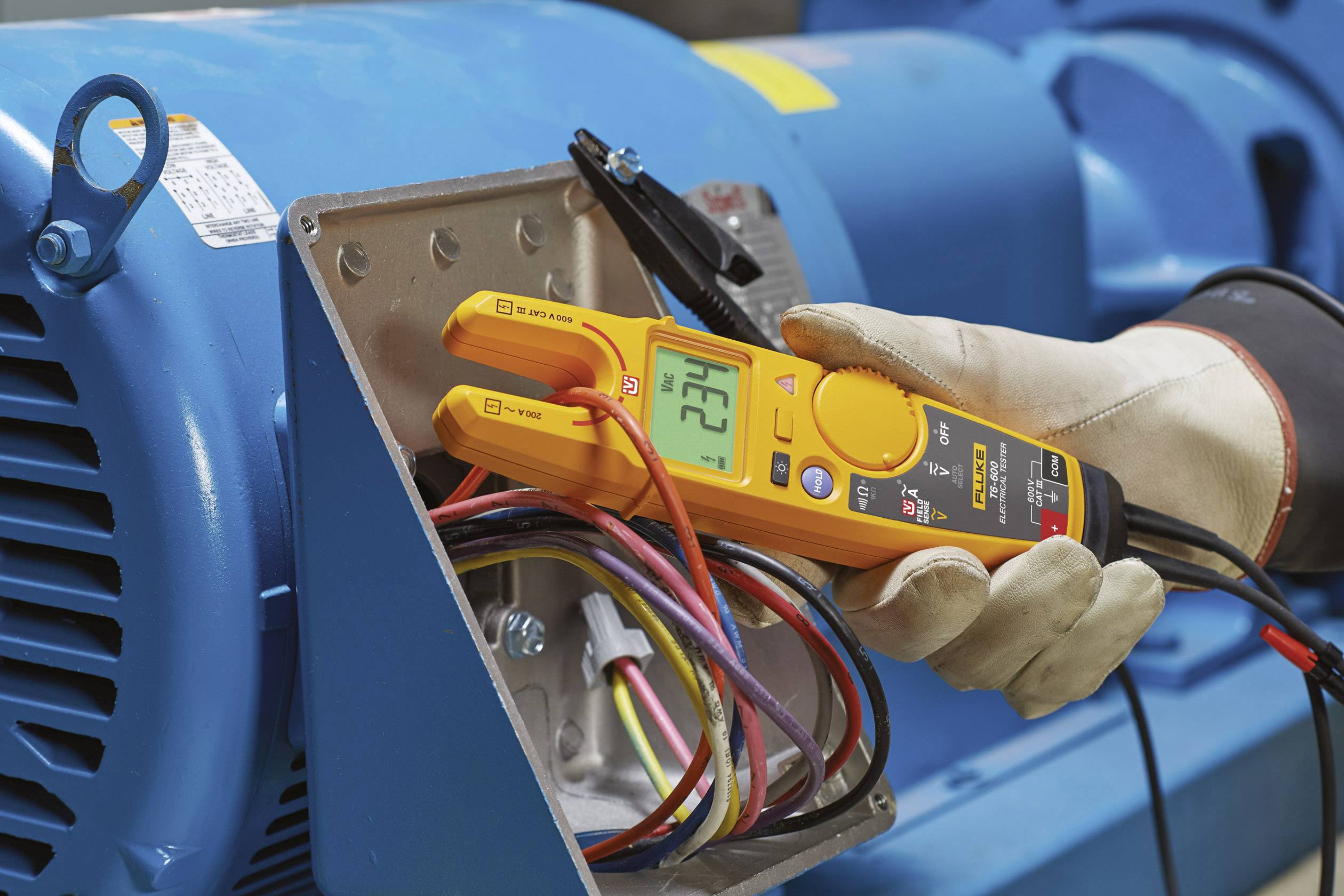 Une personne mesure la tension à l'aide d'un voltmètre numérique sur un moteur électrique ouvert. Les câbles et les connexions sont visibles.