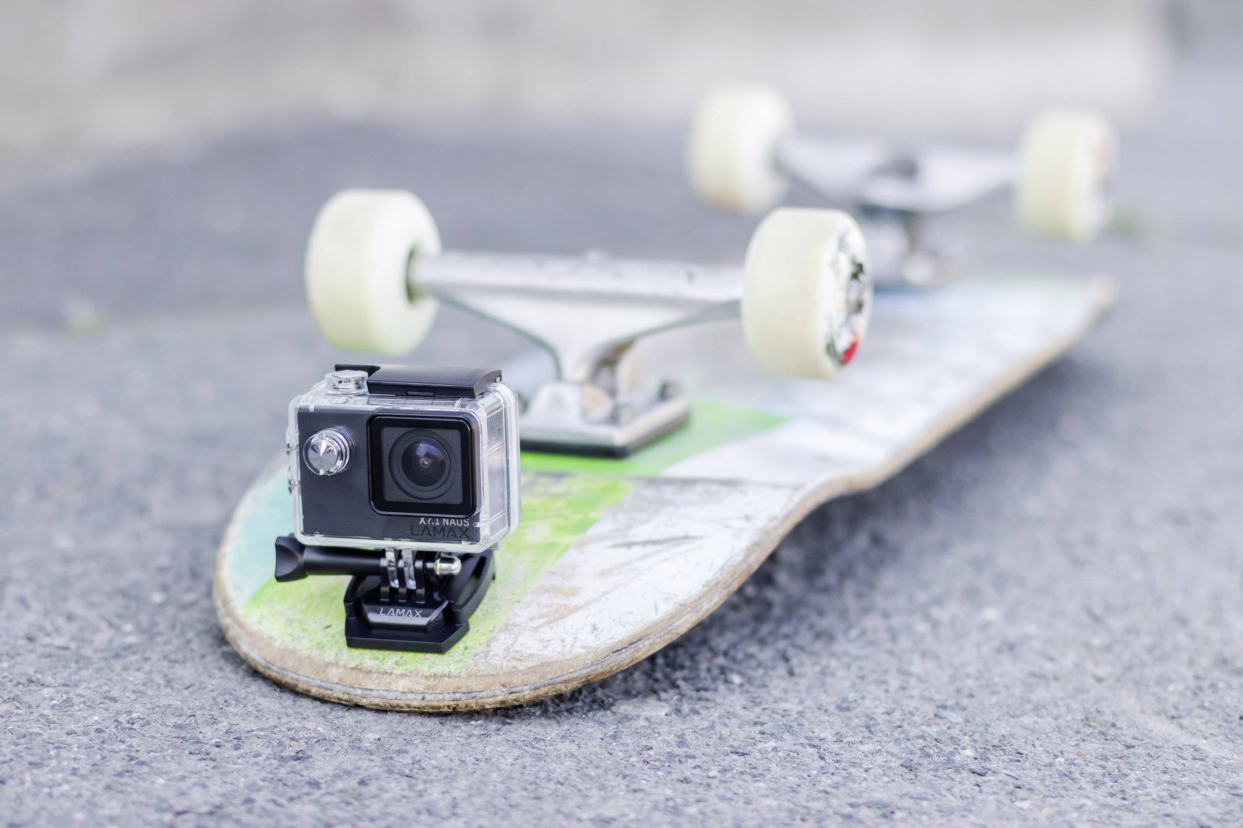 Une caméra d'action est fixée à l'avant d'une planche de skateboard posée sur un sol en béton.