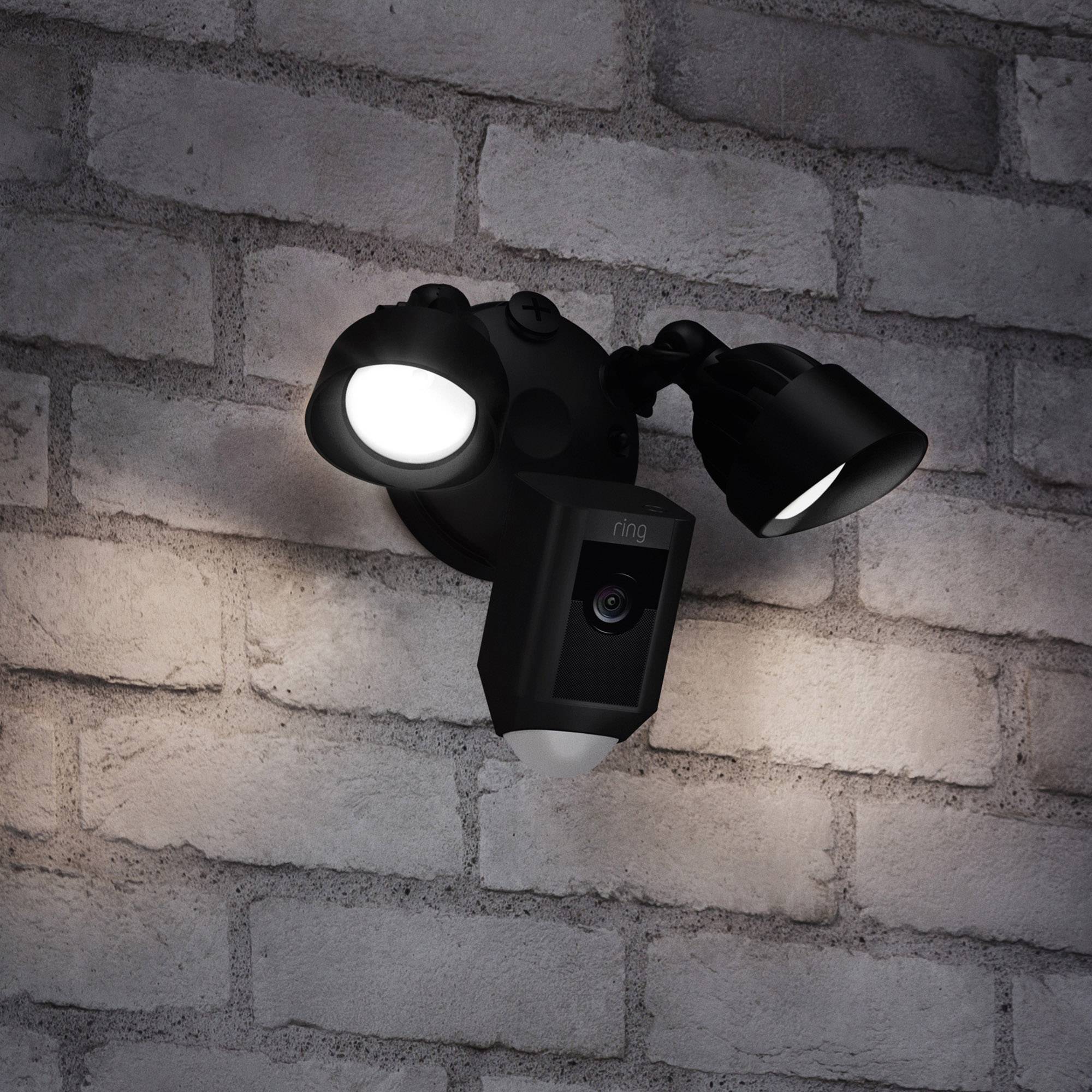 Caméra de sécurité montée sur un mur de briques, équipée de deux projecteurs LED lumineux, conçue pour la surveillance et l'éclairage.