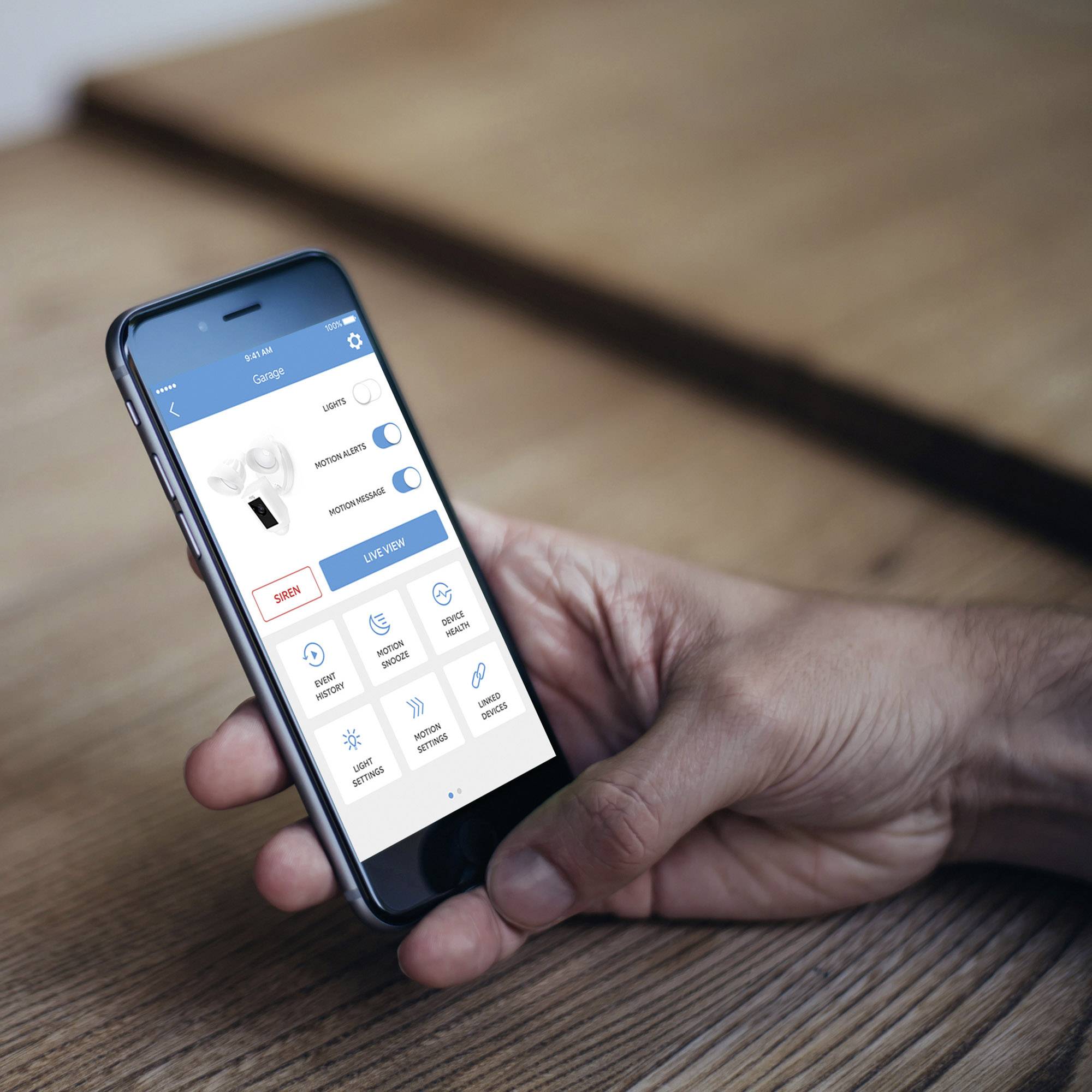 Une main tient un smartphone avec une application de contrôle d'appareil. L'application affiche une image d'un gadget et des boutons de paramètres.