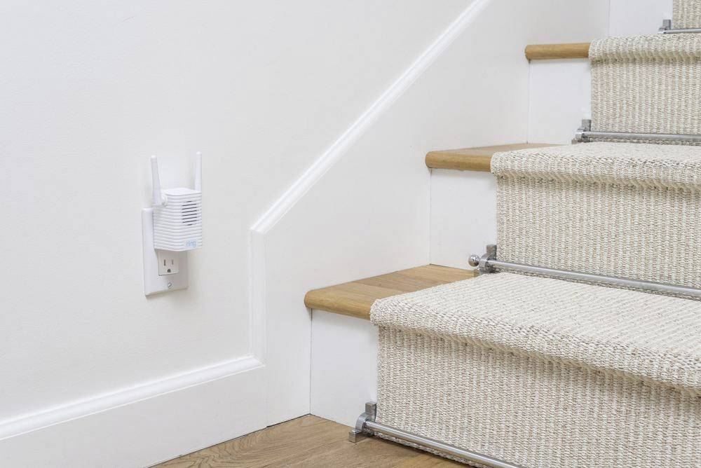 Escalier recouvert d'un tapis beige ; un amplificateur Wi-Fi installé sur le mur à côté améliore la connexion internet dans la maison.