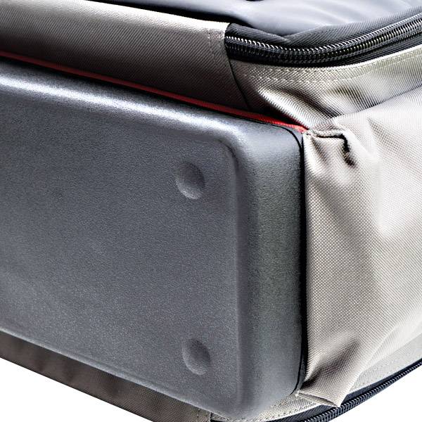 Gros plan sur une valise avec un coin de protection rigide. Le tissu est gris, avec une couture soulignée en rouge.