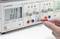 Une main tient une sonde de test rouge sur un bloc d'alimentation de laboratoire. L'affichage indique 11,9 V, 0,00 A. Régulateurs de tension et de courant, différentes connexions visibles.