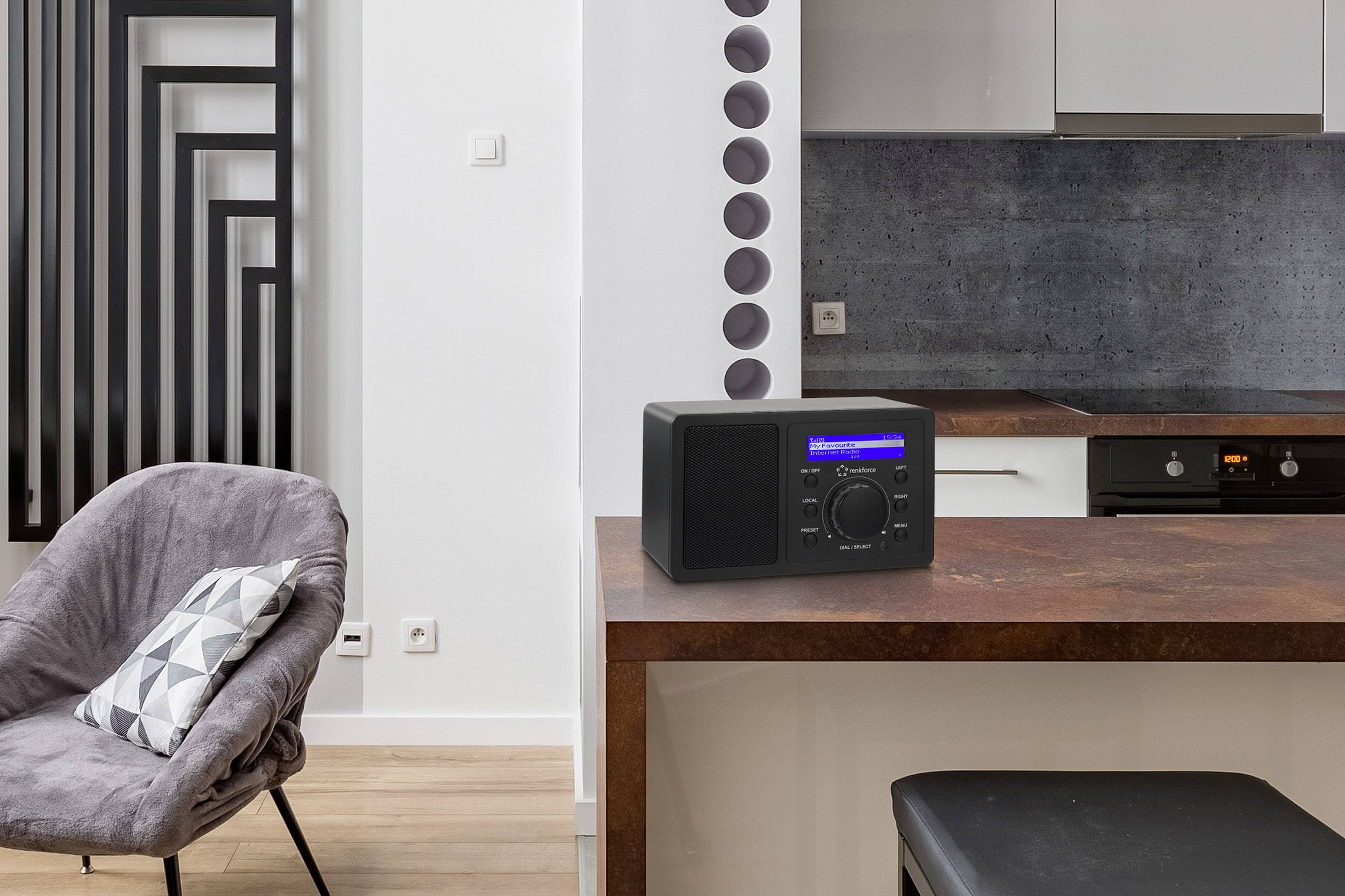 Un radio noir avec un affichage rétroéclairé est posé sur un plan de travail de cuisine. En arrière-plan, un design de cuisine et d'espace de vie moderne.