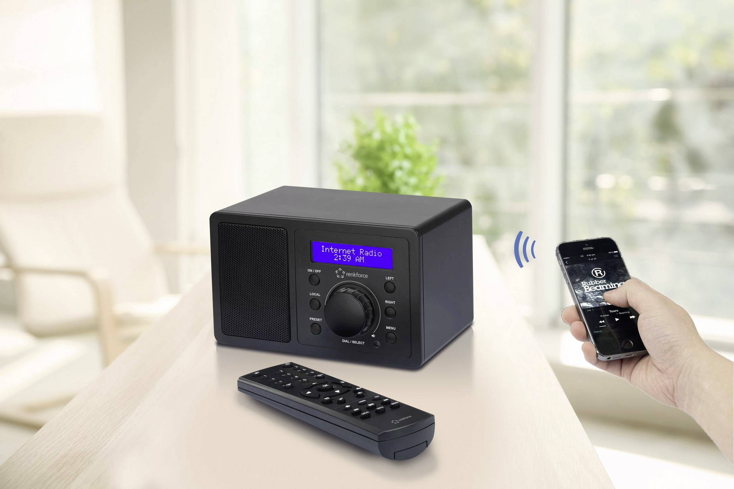 Une radio internet posée sur une table, connectée à un smartphone, affichant 'Radio Internet' sur son écran. Une fenêtre en arrière-plan.
