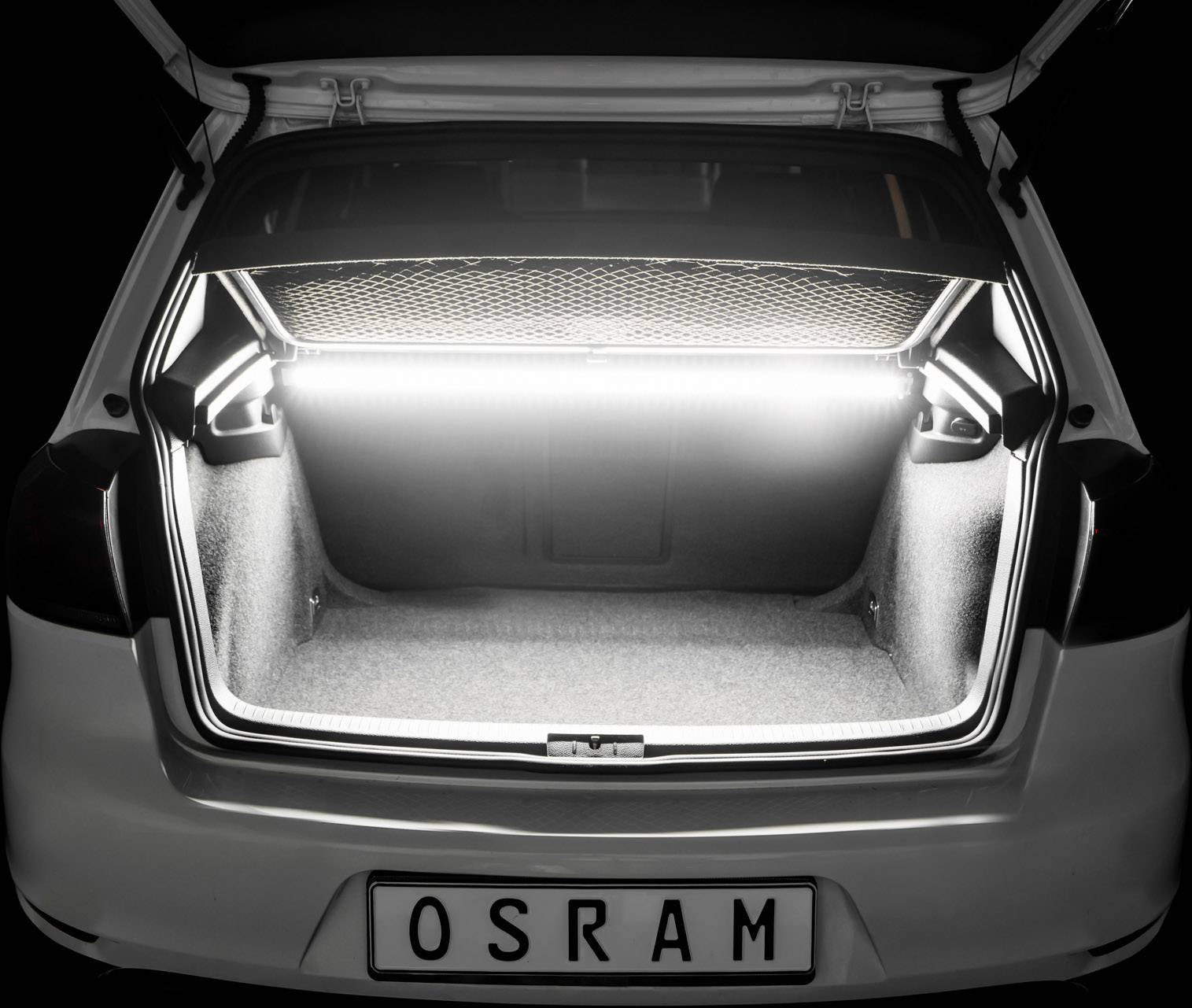 Une voiture avec le coffre ouvert. Le coffre est bien éclairé, avec un filet de protection en haut. La plaque d'immatriculation indique 'OSRAM'.