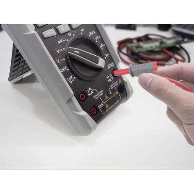 Une personne utilise un multimètre numérique pour effectuer des mesures électriques. L'échelle affiche différentes options de mesure.