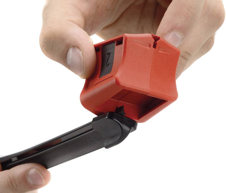 Une main tient un dénudeur de câble rouge, tandis qu'une autre main soulève le capuchon rouge à l'extrémité pour dévoiler l'outil.