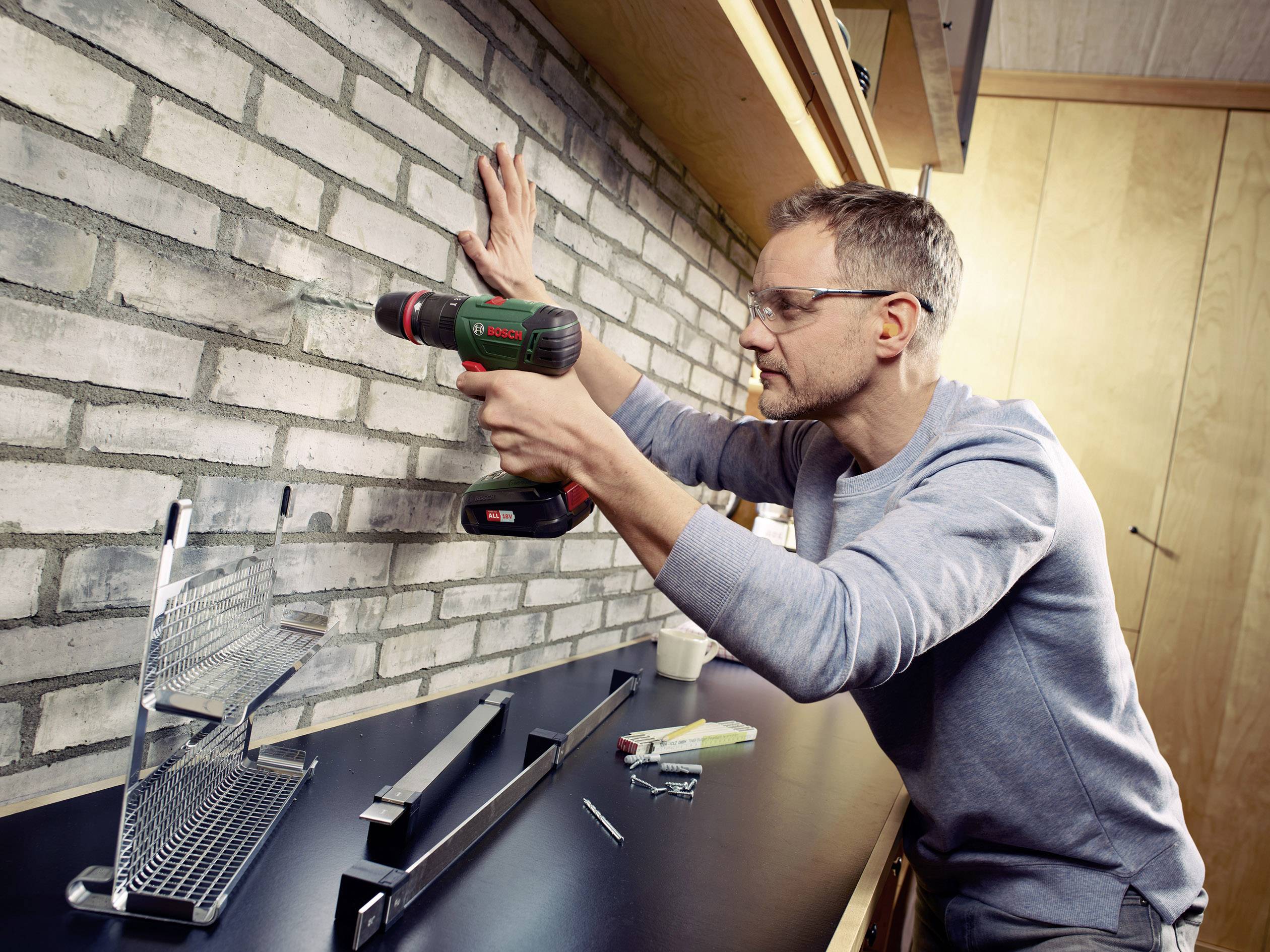 Un homme utilise une perceuse électrique pour percer un trou dans un mur de briques. Espace de travail avec des outils en arrière-plan.