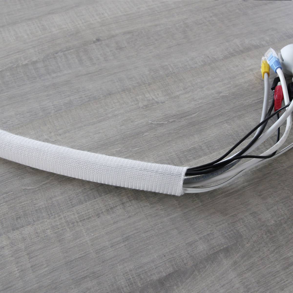 Un tuyau tressé en matériau blanc posé sur une table en bois, utilisé pour regrouper et maintenir ensemble plusieurs câbles de différentes couleurs.