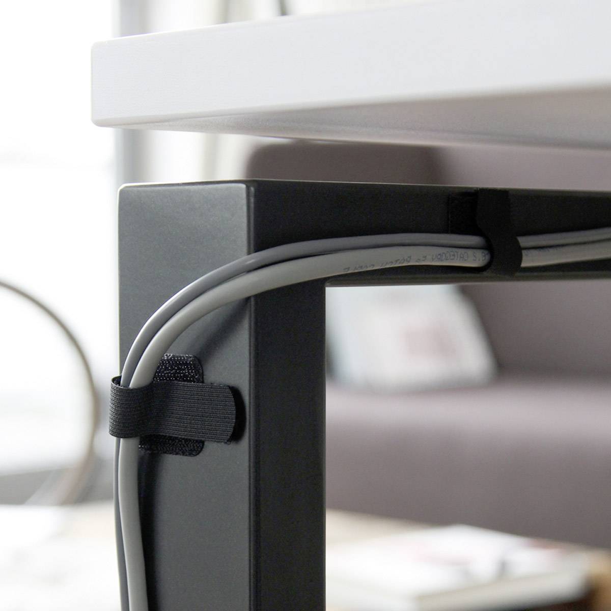 Un système de gestion des câbles fixe les câbles de manière organisée sous un bureau, créant ainsi un environnement de travail ordonné.