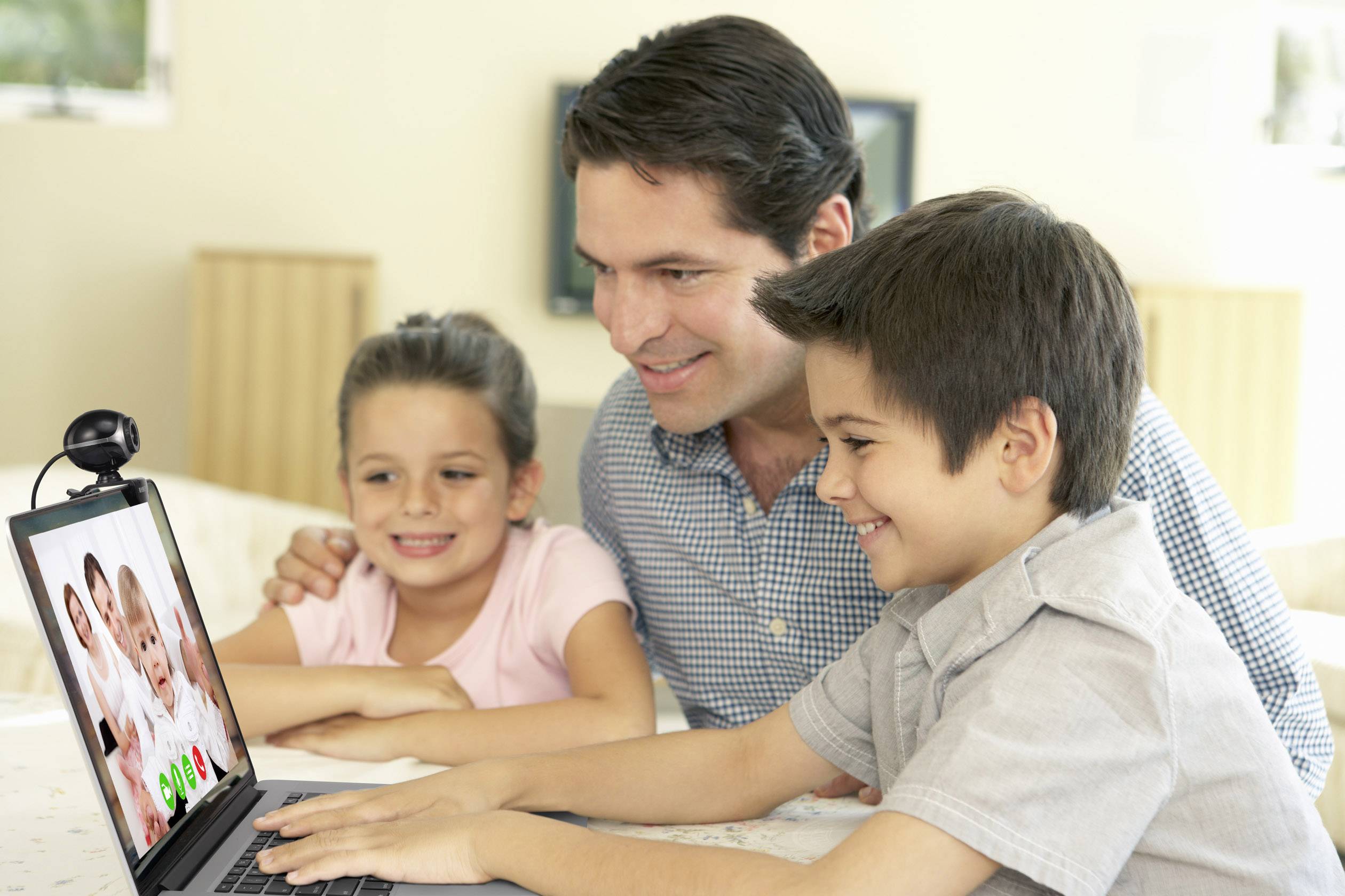 Un homme et deux enfants sont assis devant un ordinateur portable et sourient. Sur l'écran, on peut voir un appel vidéo avec deux personnes.