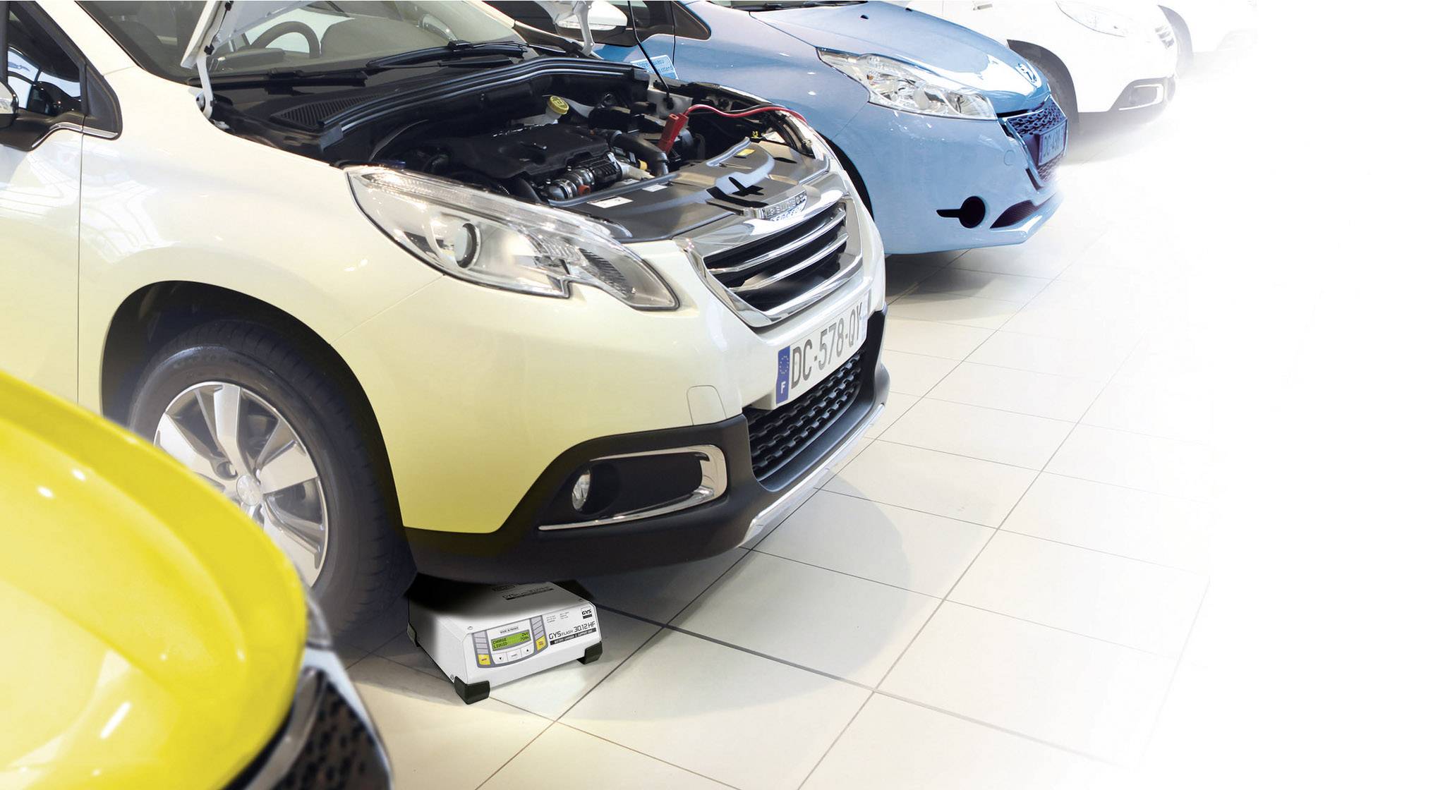 Une voiture est stationnée avec le capot ouvert dans un atelier. Un appareil est placé sous le moteur pour effectuer un diagnostic.