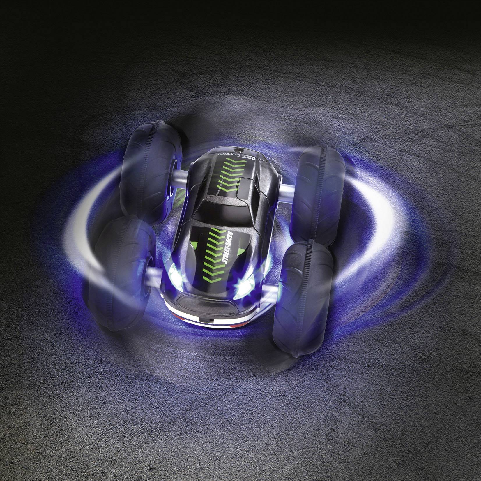 Une voiture télécommandée effectue un mouvement rotatif sur une surface sombre, avec des lumières de pneus et des phares allumés.