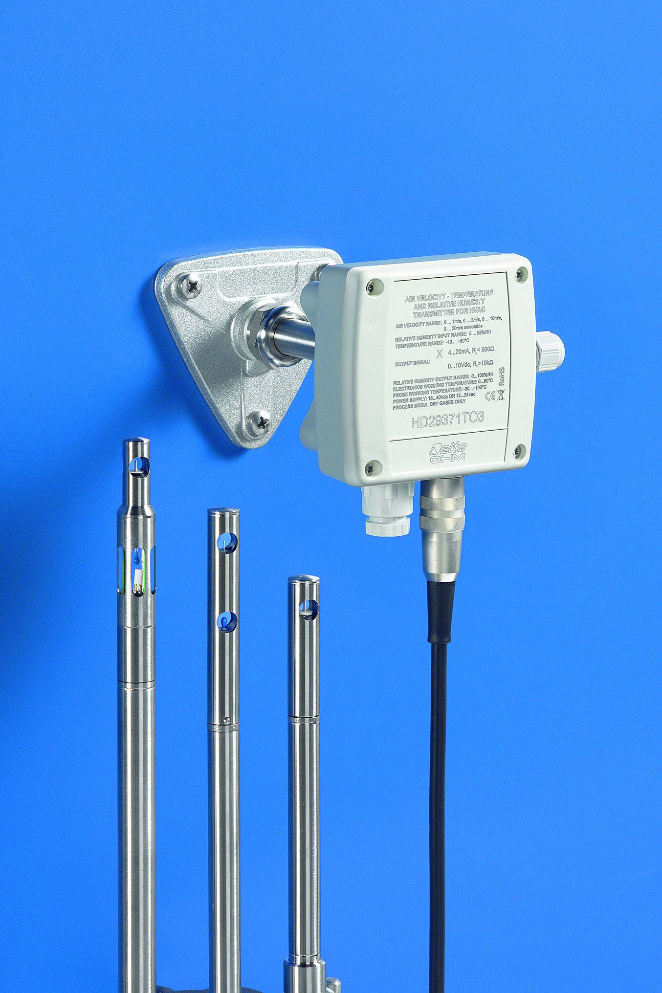 Capteur industriel, monté sur un mur bleu, avec plusieurs éléments de sonde métalliques. Dispositif de collecte et de transmission de données technologiques.