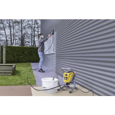 Un homme peint la façade d'une maison avec un pistolet à peinture. Une machine à peindre jaune est posée sur une table à côté de lui.