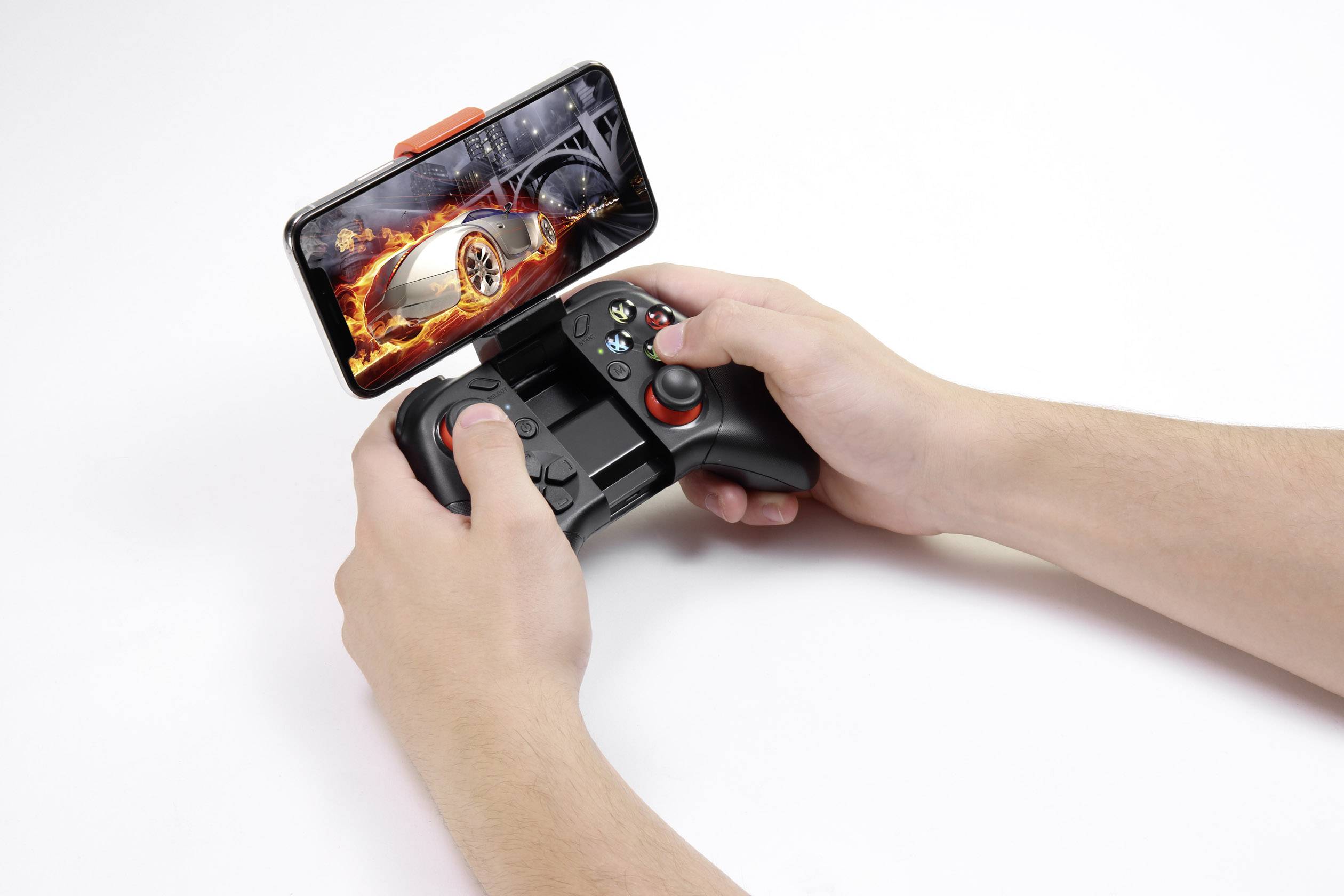 Une personne tient une manette de jeu avec un smartphone inséré. Sur l'écran, on peut voir un jeu de course automobile avec une voiture en feu.