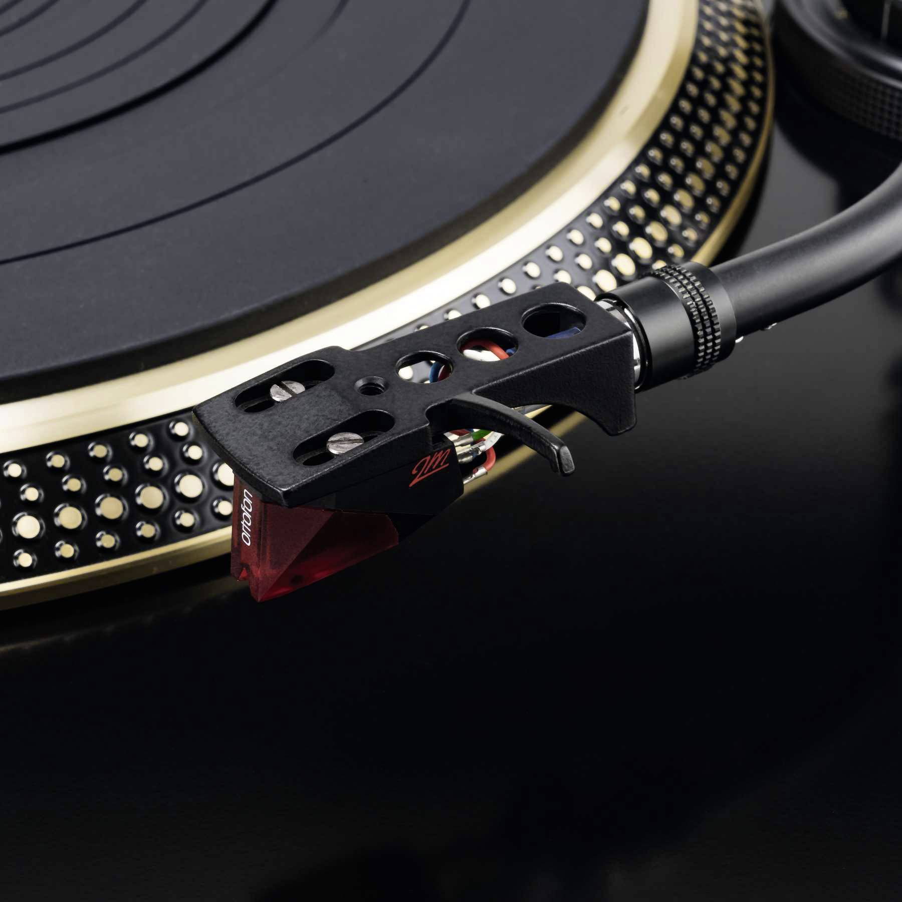 Gros plan d'une platine vinyle avec un bras de lecture en métal reposant sur une surface de plateau avec un motif pointillé.