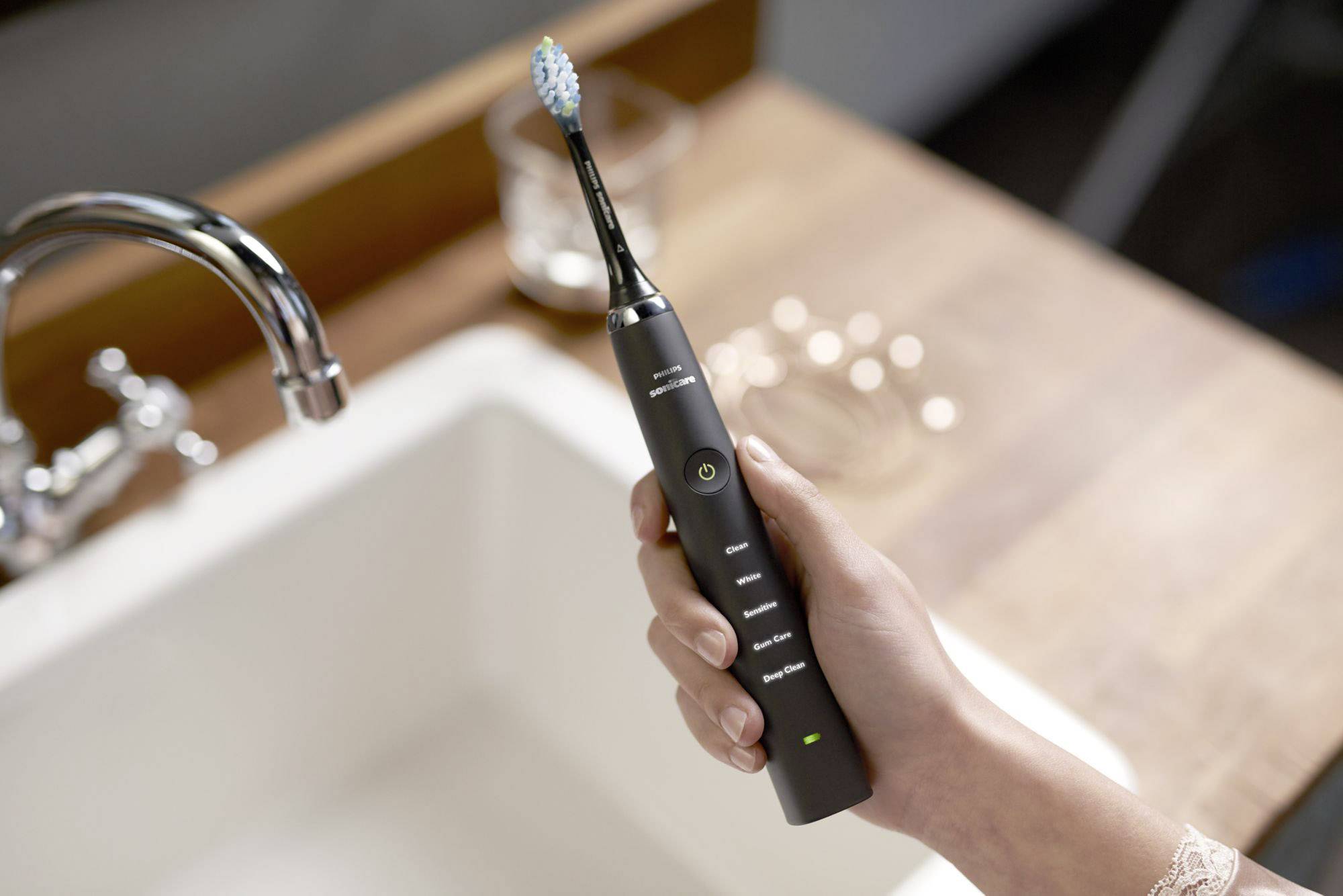 Une personne tient une brosse à dents électrique moderne au-dessus d'un lavabo. La brosse à dents présente un design élégant et est de couleur noire.