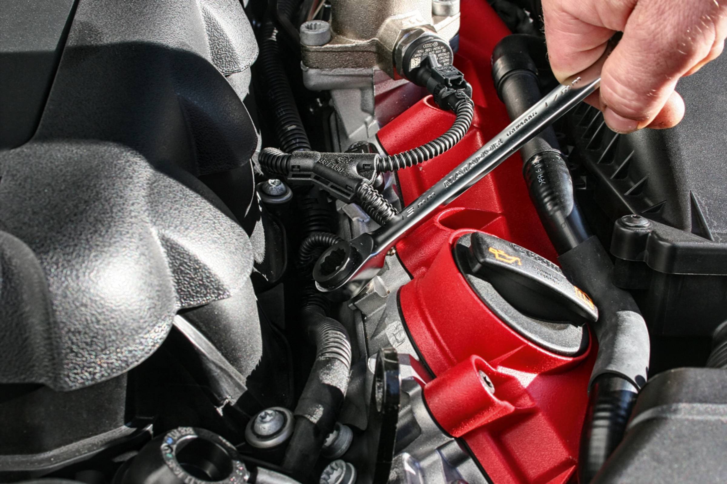 Une main tient une clé à molette et travaille sur une pièce rouge d'automobile dans le compartiment moteur.