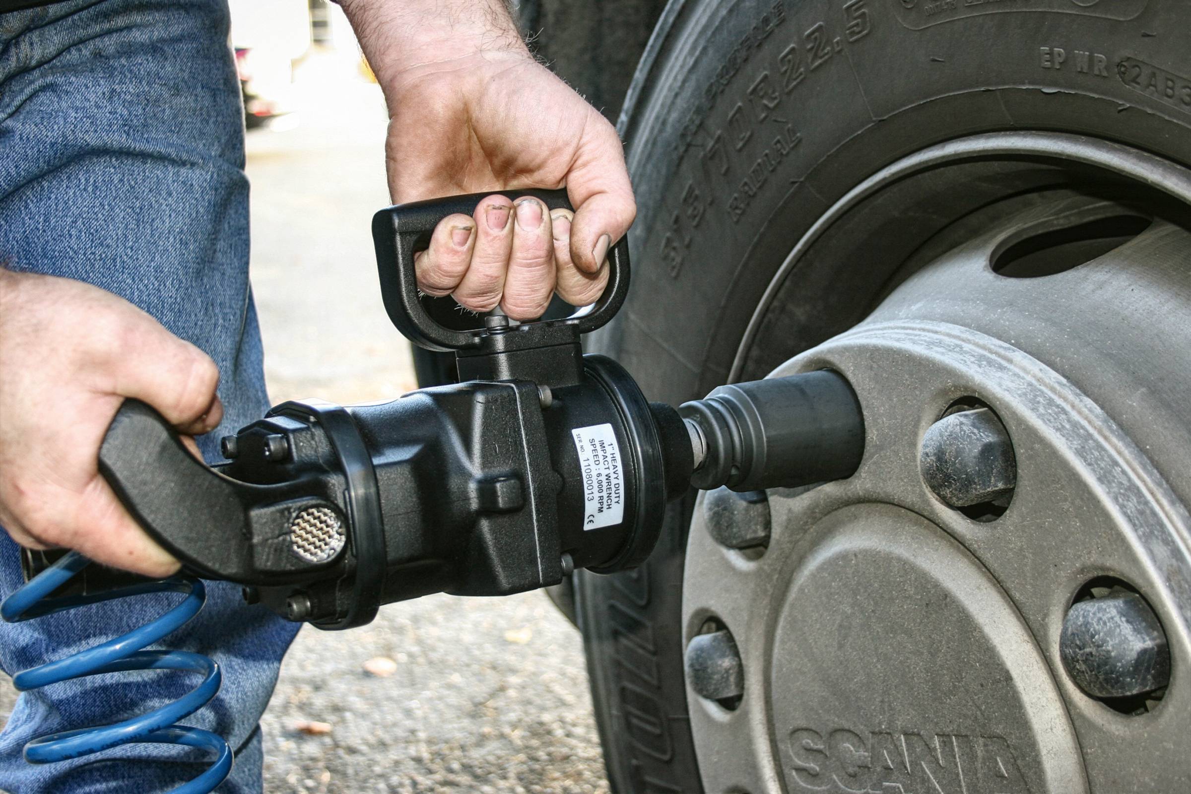 Une personne serre les écrous de roue d'un grand pneu de véhicule à l'aide d'un visseuse pneumatique. Le pneu est monté sur un camion.