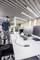 Un homme se tient dans un bureau moderne, regardant son smartphone. Au premier plan, un bureau avec deux écrans et une chaise de bureau sont visibles.