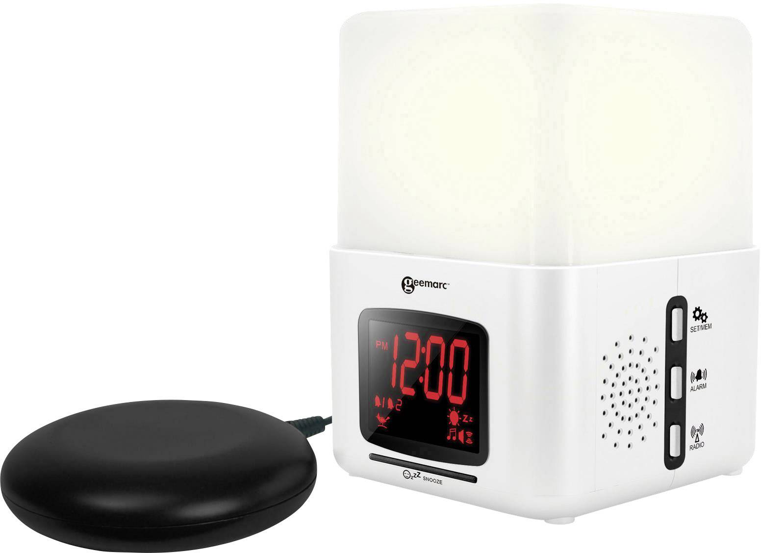 Réveil radio avec lumière blanche en haut, affichage numérique de l'heure '12:00' en rouge, réglage du volume et interrupteur. Coussin de vibration noir à côté.