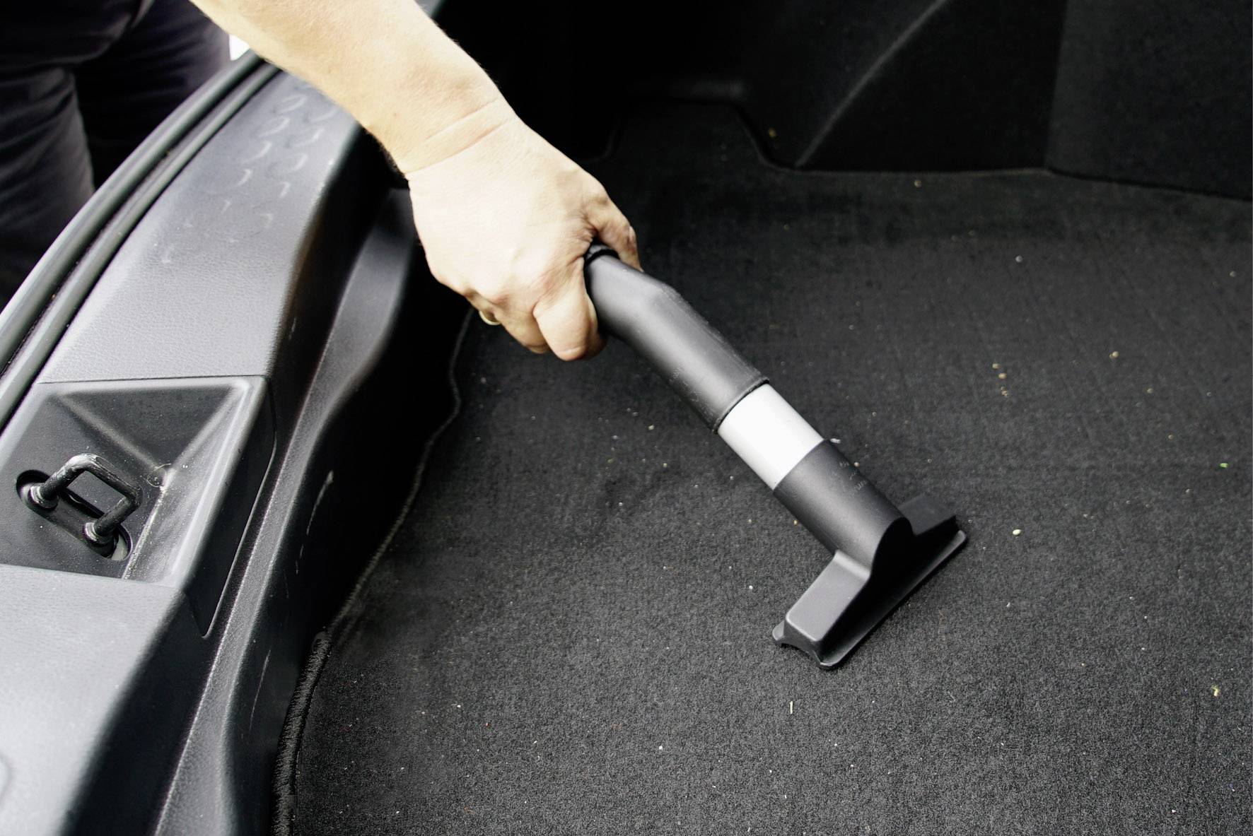 Une personne nettoie le coffre d'une voiture avec un aspirateur.