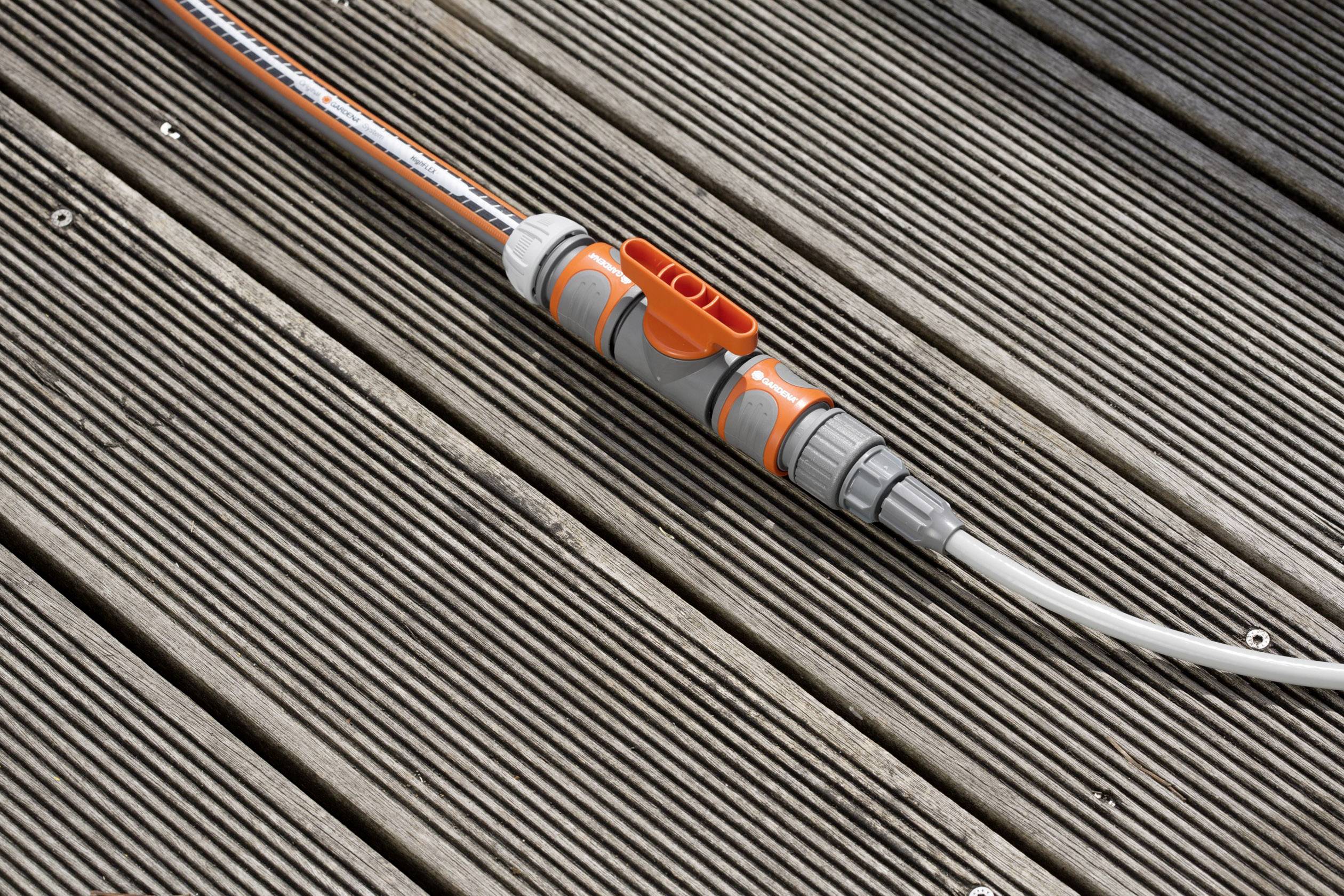 Un convertisseur de tuyau d'arrosage orange et gris est posé sur une terrasse en bois.