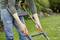 Une personne en jeans conduit une tondeuse à gazon dans un jardin. Elle tient fermement la poignée et la pelouse est bien entretenue.