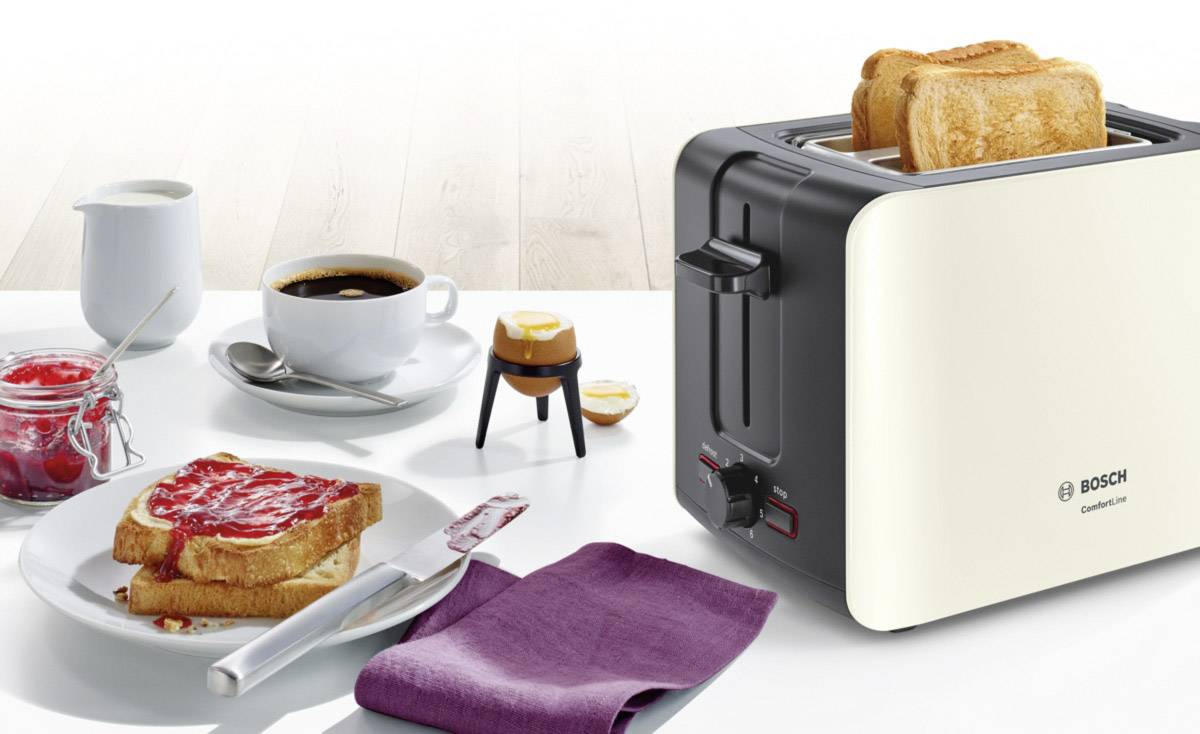 Une table de petit-déjeuner avec un grille-pain toastant deux tranches de pain, à côté du café, de la confiture et du pain grillé sur une assiette.